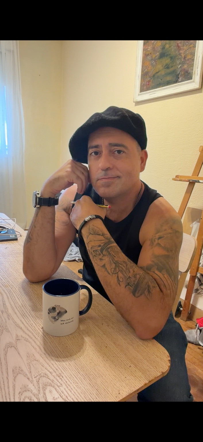Antonio Ortega sentado ante una mesa con lápiz y taza, junto a un caballete.